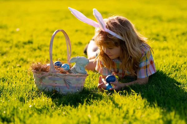 Criança a caçar ovos de Páscoa. Criança bonito em traje de coelho com orelhas de coelho tendo Páscoa no parque. Crianças caçam páscoa ovo. — Fotografia de Stock