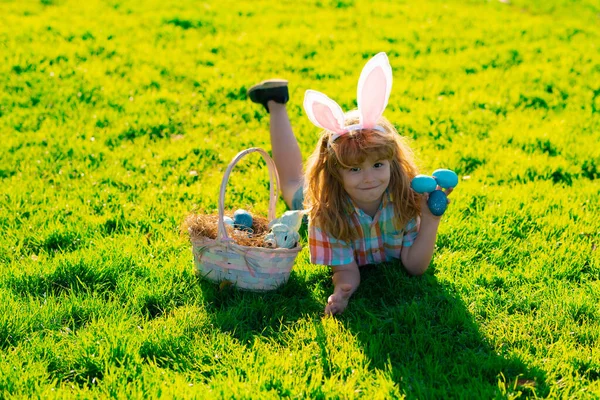 Niño con traje de conejo con orejas de conejo cazando huevos de Pascua en el parque. Vacaciones de primavera. — Foto de Stock