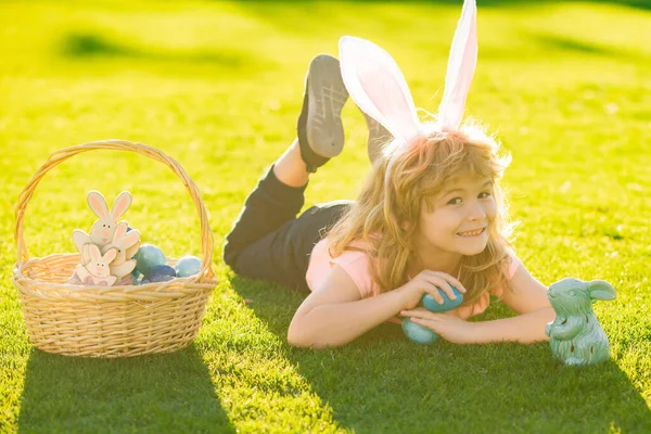 Pasen kinderen jongen in konijnenoren jagen paaseieren buiten. Schattig kind in konijnenkostuum met konijnenoren die plezier hebben in het park. Kinderen in konijnenoren op paaseieren jacht in de tuin. — Stockfoto