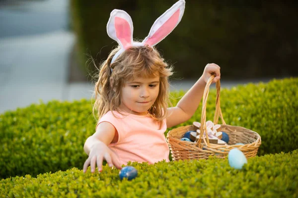 Niños en orejas de conejo en la búsqueda de huevos de Pascua en el jardín. Niño recogiendo huevos, concepto de caza de huevos de Pascua. Feliz cara de niños de Pascua. —  Fotos de Stock