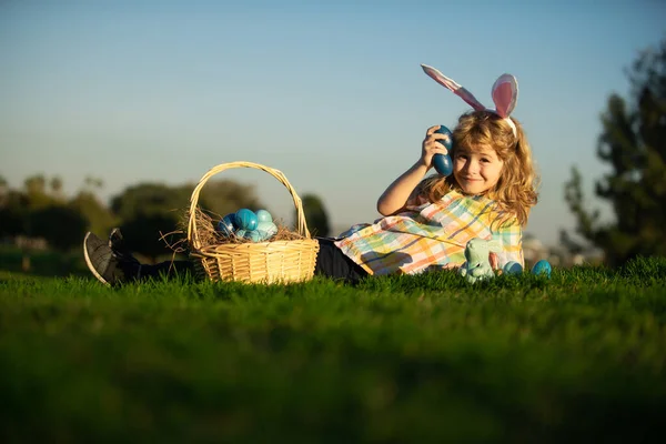 Tavşan kulaklı şirin tavşan çocuk. Paskalya yumurtası ve çimlerin üzerinde sepeti olan çocuk. Paskalya yumurtası avlayan, çimlerin üzerinde yatan çocuk. Gökyüzündeki Paskalya tavşanı çocukları için kopya alanı. — Stok fotoğraf