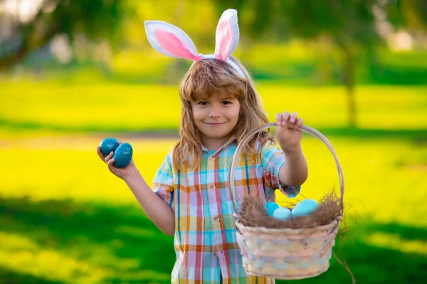 Boldog Húsvétot a gyerekeknek. A kisfiú húsvéti tojásra vadászik. Gyermek fiú húsvéti tojás és nyuszifül a parkban. — Stock Fotó