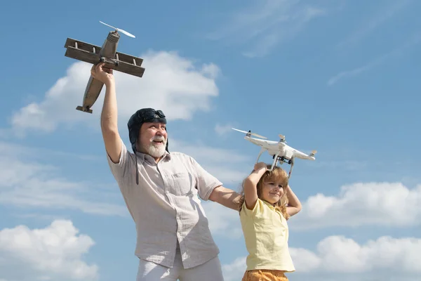 祖父と孫は空に対して飛行機とドローンのクワッドコプターを保持します。飛行機の夢を持つ子供パイロット航空機. — ストック写真