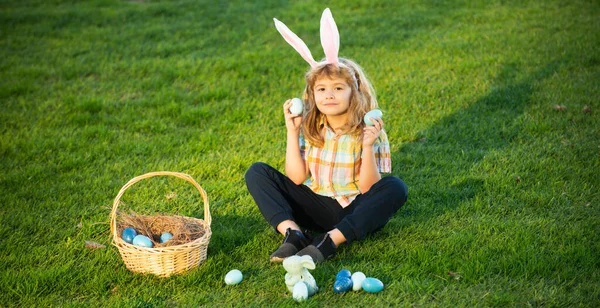 Konijnenkinderen met konijnenoren. Kids jongen jagen paaseieren in het park leggen op gras. — Stockfoto