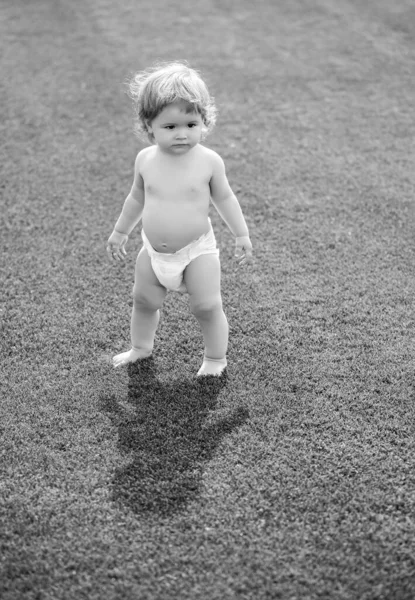 Liebenswerter kleiner Junge im Freien, der auf grünem Gras posiert. Sommerporträt eines schönen Kindes auf dem Rasen. — Stockfoto