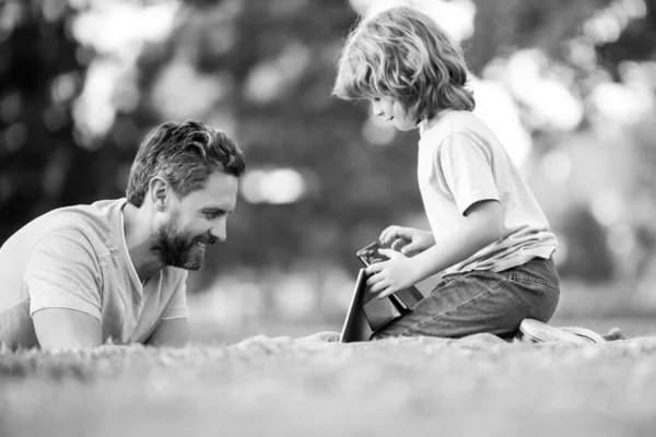 Père heureux utilisant ordinateur portable se détendre avec le fils écolier tenant ordinateur portable s'amuser ensemble, souriant papa et petit garçon enfant profiter week-end avec des gadgets à l'extérieur sur la nature. Appel vidéo d'un petit-fils aux parents. — Photo