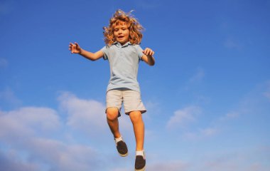 Parkta koşan ve mavi gökyüzünde gülümseyen beyaz bir çocuk. Mutlu çocuk gülüyor. Duygu, neşe çocuğuyla yüzleşir. Neşeli, eğlenceli bahar, yaz günü, açık havada. Gökyüzü arkaplanı, kopyalama alanı olan pankart.