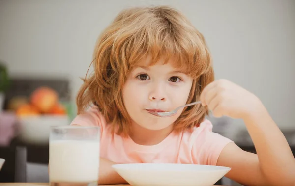 Een close-up gezicht van een kind dat biologisch voedsel eet, yoghurt, melk. Kind gezond eten. glimlachend jongetje eten op keuken. — Stockfoto