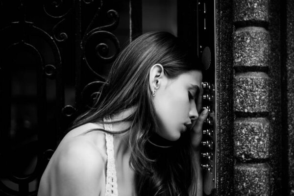 Sad pensive woman in depression. Self isolation. Home safety concept. Woman intercom code button. Lady female doorbell at building entrance.