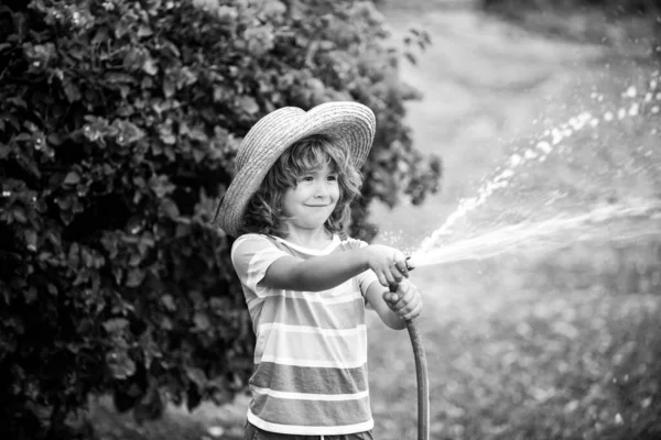 Aranyos srác szalmakalapban nevet a vízpermetező tömlővel. — Stock Fotó