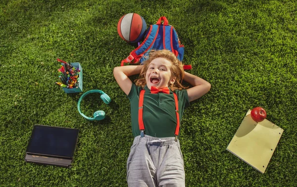 Aufgeregte Kinder lernen online in der virtuellen Schule mit Tablet auf grünem Gras im Freien, E-Learning. Glücklicher Junge entspannt sich auf dem Rasen. — Stockfoto