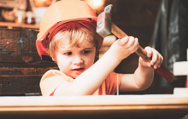 Kid in hard hat holding wooden plank and hammer. Child engineer with carpenter work hammer on wood. — Stock Photo, Image