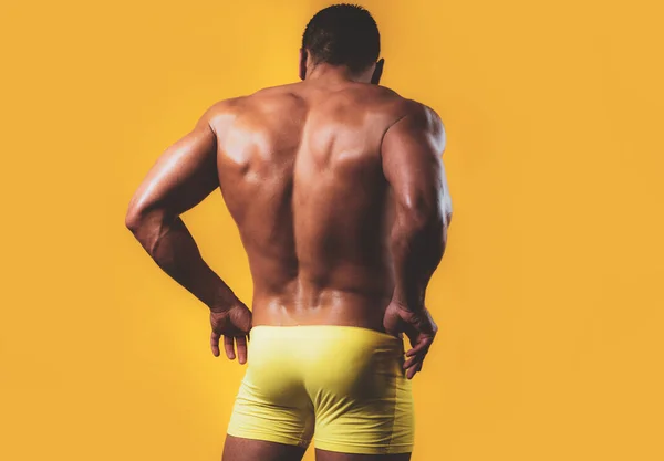 Sexy man terug. Het achteraanzicht van romp van aantrekkelijke mannelijke bodybuilder op gele achtergrond. Achteraanzicht van een kale borst gespierde jonge man in sexy slipje ondergoed. — Stockfoto