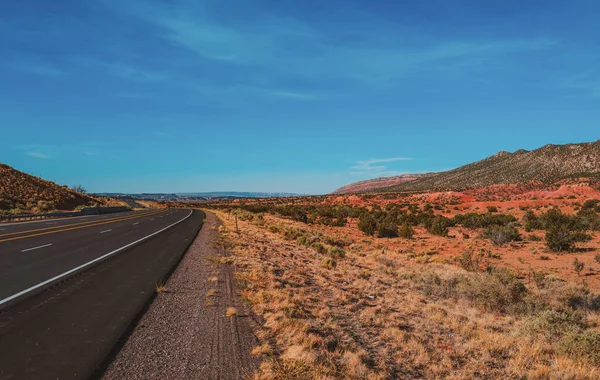 Snelweg die door het onvruchtbare landschap van het Amerikaanse zuidwesten loopt met extreme hitte op een hete zonnige dag met blauwe lucht in de zomer. — Stockfoto