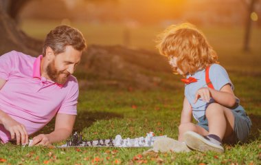Baba ve oğul parkta birlikte satranç oynuyorlar. Aktif insanlar parkta satranç oynayıp eğleniyorlar, çocuklarla vakit geçiriyorlar..
