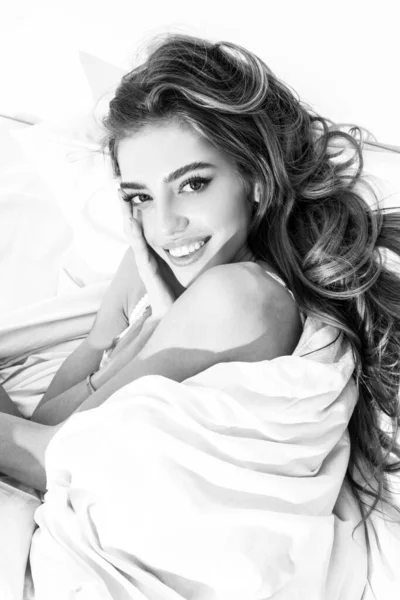 Lächelnde sinnliche Frau, die im Bett unter einer Bettdecke im Schlafzimmer liegt. Guten Morgen. — Stockfoto