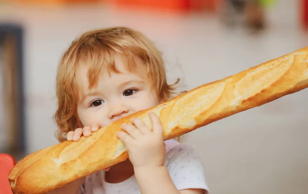 Lindo bebé comiendo pan blanco baguette francés. Divertido niño pequeño comiendo sándwich, concepto de autoalimentación. — Foto de Stock