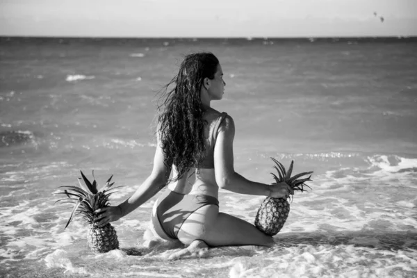 Female buttocks in thongs bikini, sexy ass. Young woman holding a pineapple on sea sand beach background. — Stockfoto
