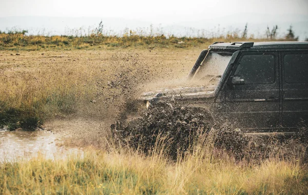 Nízký úhel pohledu před SUV na horské silnici. Terénní džíp na špatné štěrkové cestě. Bahno a voda stříkání v off-road závodech. — Stock fotografie