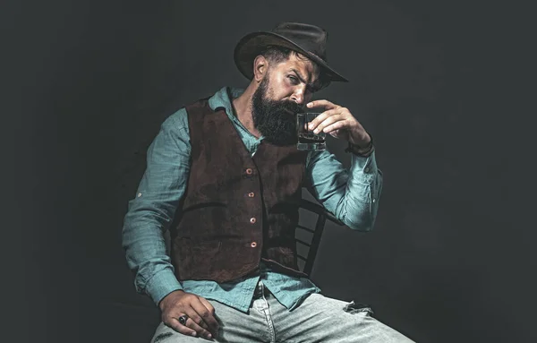 Der elegante, bärtige Barkeeper hält ein Whiskeyglas in der Hand. Konzept für Luxusgetränke. Modischer Mann in weißem Hemd und Hosenträgern. — Stockfoto