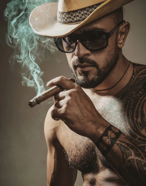 Verleidelijk gezicht van een sexy man die sigaar rookt. Macho lijkt zelfverzekerd. Getatoeëerde en elegante hipster. — Stockfoto