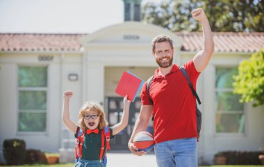 Oğlunu okula götüren harika bir baba. Sırt çantalı ilkokul öğrencisinin ebeveyni ve öğrencisi. Neşeli baba ve oğul portresi. Okulun önünde. Keyifleri yerindeydi..