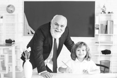 Yaşlı öğretmen ve genç öğrenci veya okul çocuğu. Öğrenci sınıfta öğretmenle okuma yazma öğreniyor..