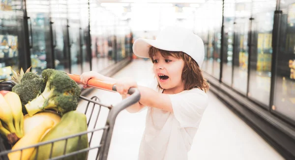 Verkauf, Konsum und Menschen-Konzept - glücklicher kleiner Junge mit Lebensmitteln im Einkaufswagen im Supermarkt. — Stockfoto