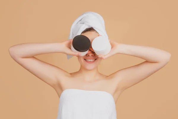 Beauty woman with cream bottle. Portrait of attractive young girl with a bath towel on head. Beautiful woman face portrait. Gestures for advertisement. Beige background — Stock Photo, Image