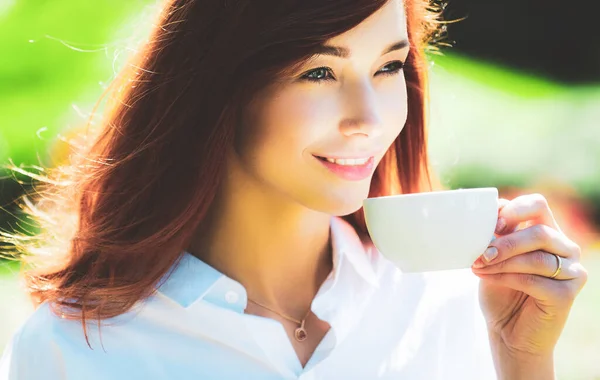 Ritratto ravvicinato di giovane bella donna che tiene la tazza di caffè del mattino su sfondo verde primavera. Felice sorridente bella giovane donna con fiori primaverili in giardino tenere tazza di caffè . — Foto Stock