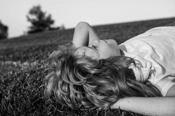 Chico alegre tendido en la hierba verde. Niños soñando. Niño feliz jugando en el campo de primavera verde contra el fondo del cielo. Concepto libertad e imaginación. — Foto de Stock