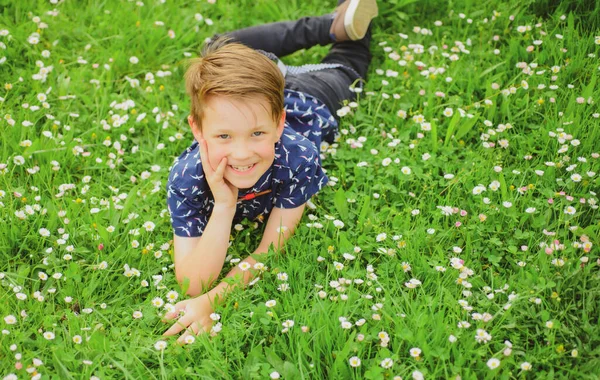 Glad bekymmerslös pojke som ligger på gräsmattan. Söt unge barn njuter på fältet blomma och drömmer. — Stockfoto