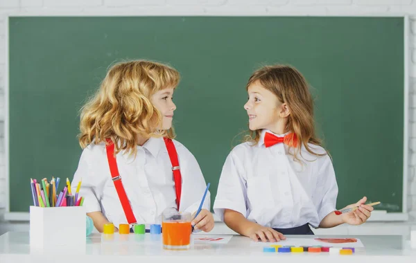 Niños haciendo clases en clase. Divertida colegiala un chico alumno dibujando un cuadro. Lindos niños de preescolar dibujando en la escuela. Amigos de la escuela. — Foto de Stock