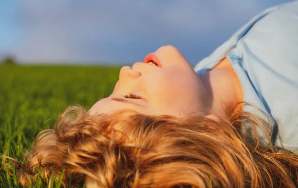 Portret van een lachend jongetje op groen gras. glimlachende jongen hebben plezier buiten in de lente tuin. — Stockfoto