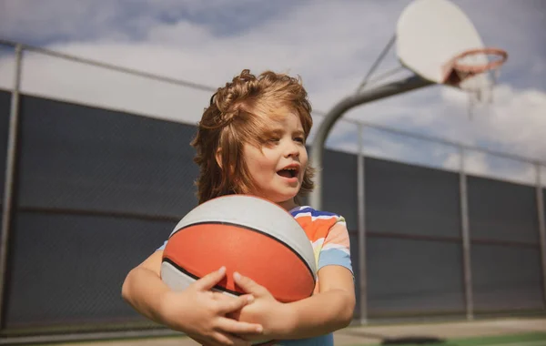 En liten kaukasisk sportunge som spelar basket med glatt ansikte. Aktiv ungdom livsstil. Porträtt av sportiga barn. — Stockfoto