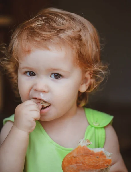 Portrait of cute baby with bread in her hands eating. Cute toddler child eating sandwich, self feeding concept. — Stock Photo, Image