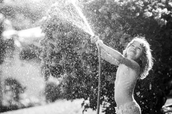 Happy little boy having fun in domestic garden. Child hold watering garden hose. Active outdoors games for kids in the backyard during harvest time — Stock Photo, Image