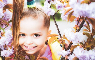 Küçük mutlu kız pembe çiçeklerle kiraz ağacının altında oynuyor. Kiraz çiçeğinin tadını çıkaran kız..