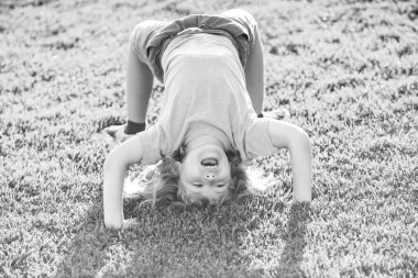 Mutlu kız çocuğu yaz günü çimlerin üzerinde baş aşağı duruyor..