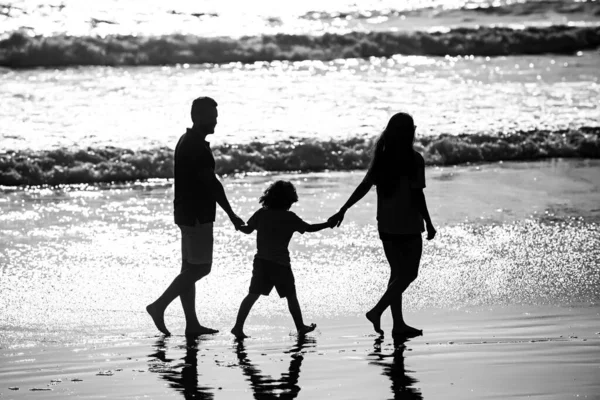 父、母、子のシルエット手を取り合いビーチを歩く. — ストック写真