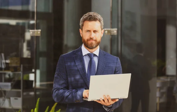 Empresario con portátil al aire libre. Experto en negocios seguro. Hombre guapo en traje sosteniendo portátil contra fondo de oficina. —  Fotos de Stock