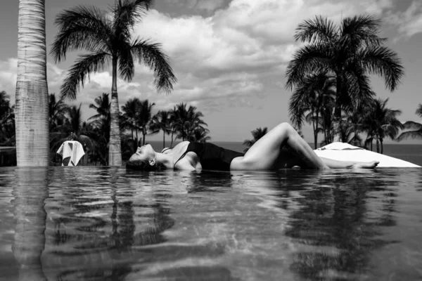 Sexy mujer elegante en la piscina infinita y disfruta de la vista sobre el mar azul. — Foto de Stock