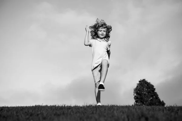 Malý chlapec utíkal a skákal po trávě poblíž jarní zelené louky na modré obloze. Happy dítě dívka hrát na slunném poli, letní příroda venkovní životní styl. — Stock fotografie