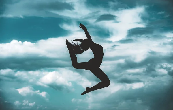 Vrouwengymnastiek silhouet. Vrouwelijke turnster op blauwe lucht achtergrond. Silhouetted turner doet de split sprong. — Stockfoto