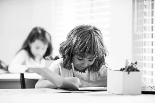 可爱的男孩在教室里画画.学校的孩子在抄本上写作，坐在教室的桌旁. — 图库照片