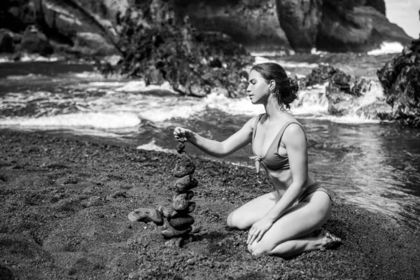 Mujer sexy haciendo pila de guijarros piedra contra el fondo del mar para spa, equilibrio, meditación y tema zen. Balance de vida y concepto de armonía. — Foto de Stock