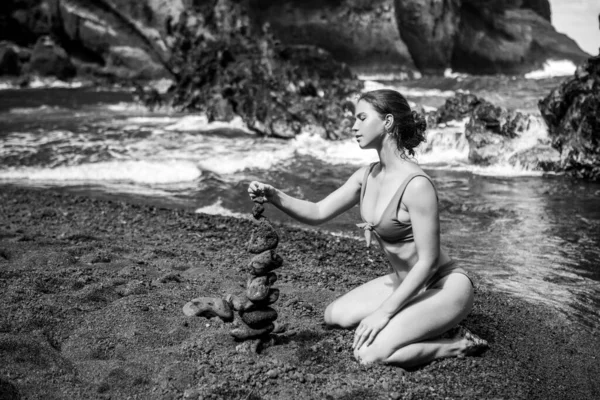 Mujer sexy haciendo pila de guijarros piedra contra el fondo del mar para spa, equilibrio, meditación y tema zen. Balance de vida y concepto de armonía. Imágenes de stock libres de derechos