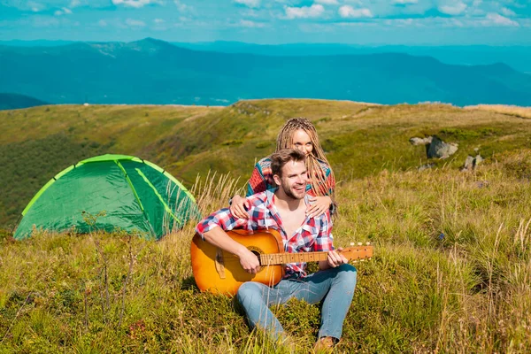 Pareja romántica acampando en paisaje primaveral. Aventura para los amantes jóvenes campistas en la naturaleza, hombre con guitarra. — Foto de Stock