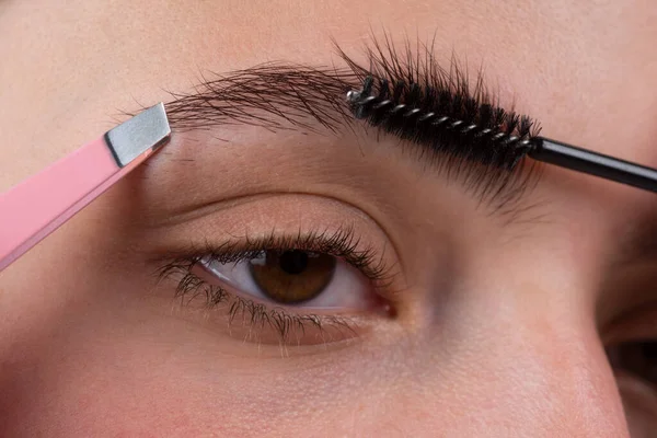 Eyebrow makeup. Macro close up of brows. Woman brushing brows with brows brush closeup. Microblading, modeling brows.