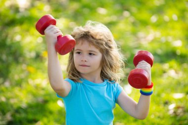 Çocuklar sabah sporu egzersizleri. Çocuklar spor yapar. Dışarıda çocuklarla boş zamanlarında spor faaliyetleri. Güzel sarışın çocuk parkta dambıllar tutuyor..